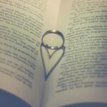 En öppen bok där en silverring ligger i mitten och en hjärtformad skugga formas i boken.