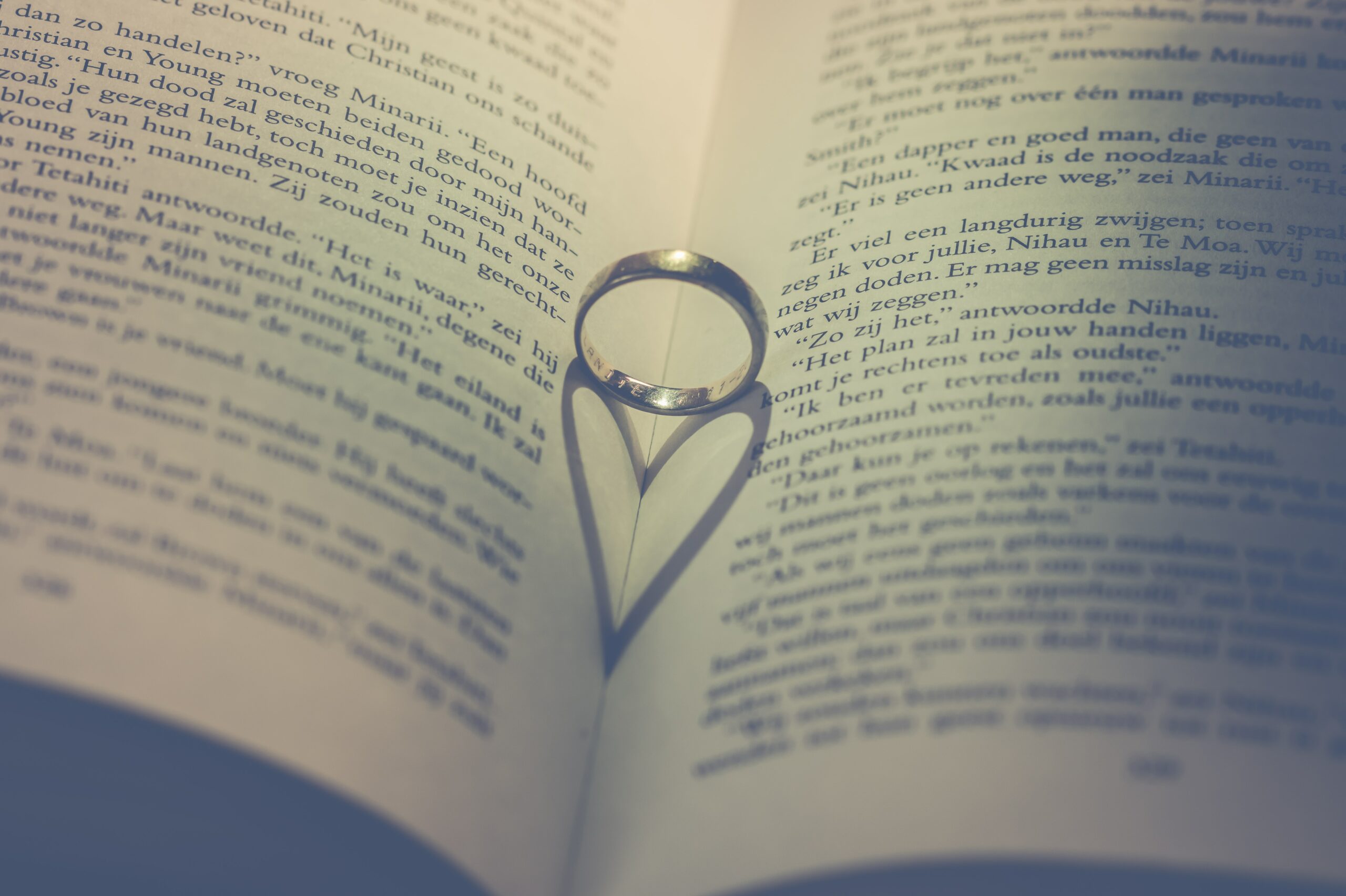 En öppen bok där en silverring ligger i mitten och en hjärtformad skugga formas i boken.