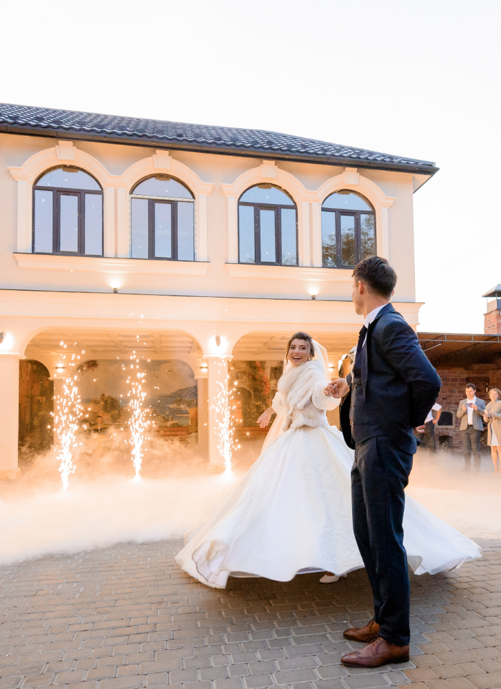 Brudpar som dansar bröllopsvals med ett beiget hus i bakgrunden