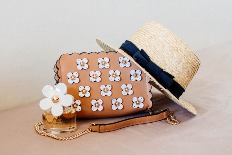 Blommig väska bredvid en beige hatt och en parfym
