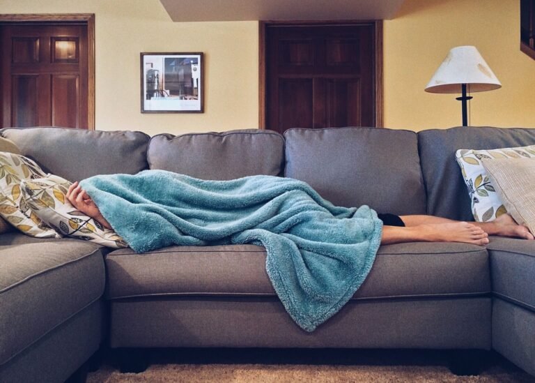 Person på en soffa som sover under en mysig blå filt